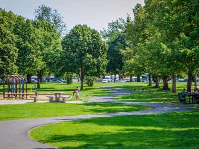 A meandering asphalt pathway runs through a lush green grass area surrounded by trees