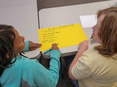 Two elementary students write answers to a question about what they are looking forward to about a new school. 