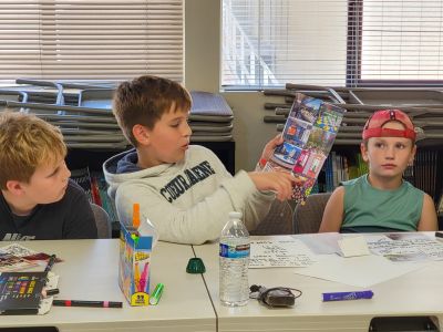 An elementary student holds up a collage of photos featuring different design ideas for  a new elementary school. 