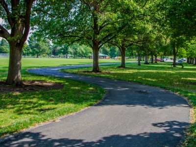 A meandering asphalt pathway runs through a lush green grass area surrounded by trees
